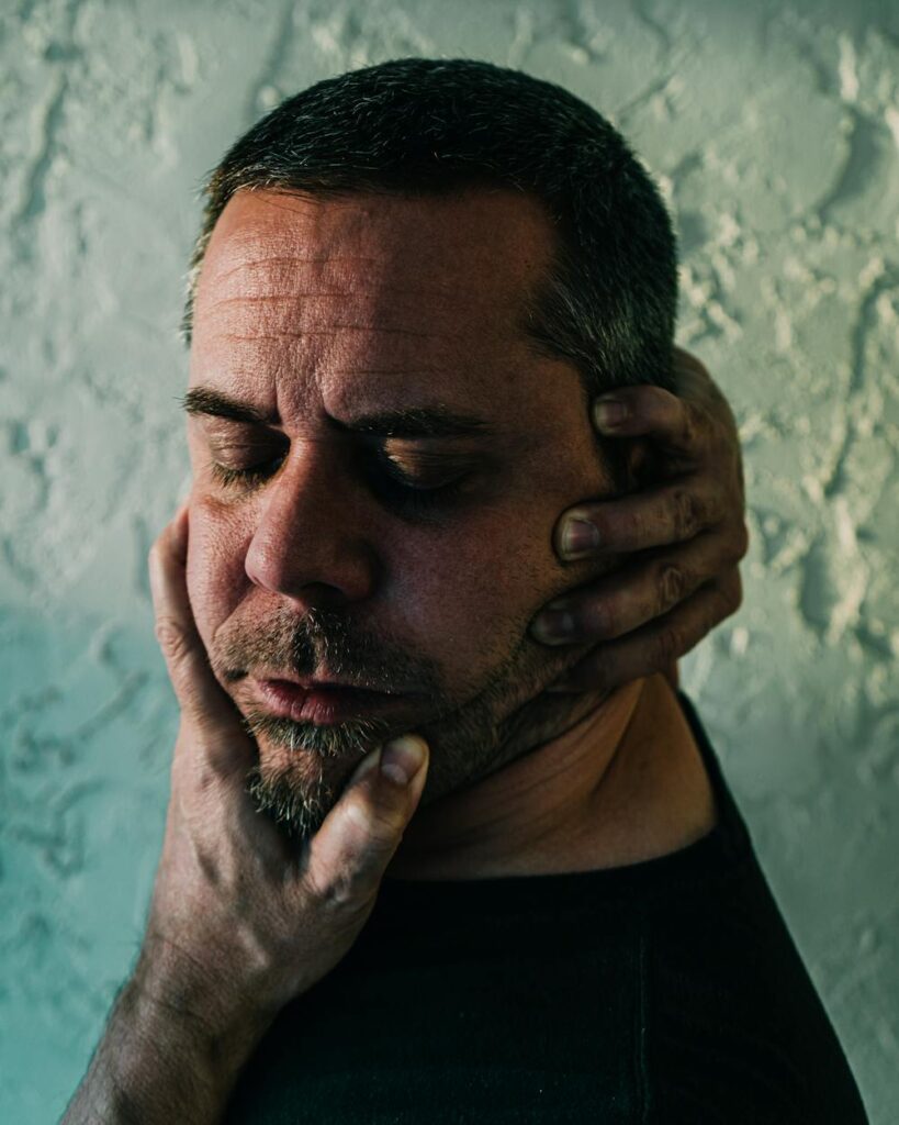 Man wincing and holding his cheek in facial pain, representing trigeminal neuralgia symptoms