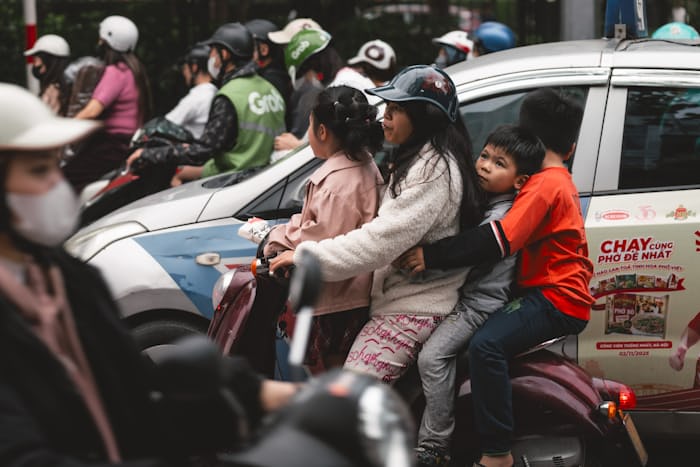 Family riding a motorbike together through traffic, showing why helmets matter for road safety in Pakistan