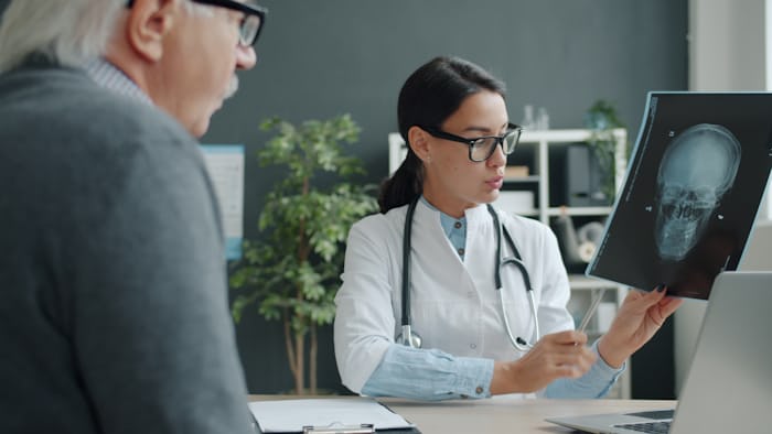 Neurosurgeon reviewing a skull scan while explaining brain tumor symptoms to a patient
