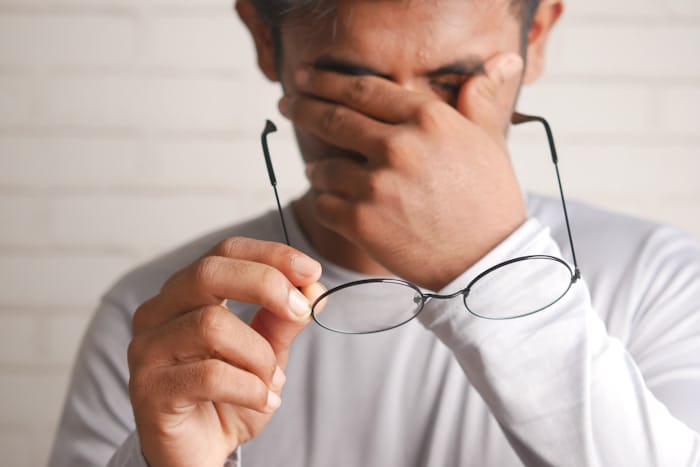 Man rubbing tired eyes at a desk, a common cause of ordinary eye twitching